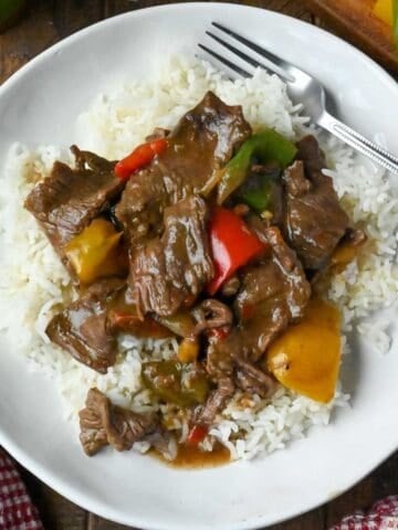 A plate of slow cooker pepper steak served over white rice.