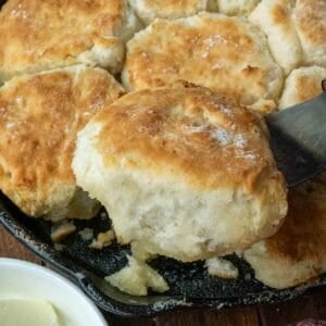 Using a spatula to lift a 7-up biscuit from a cast iron skillet.