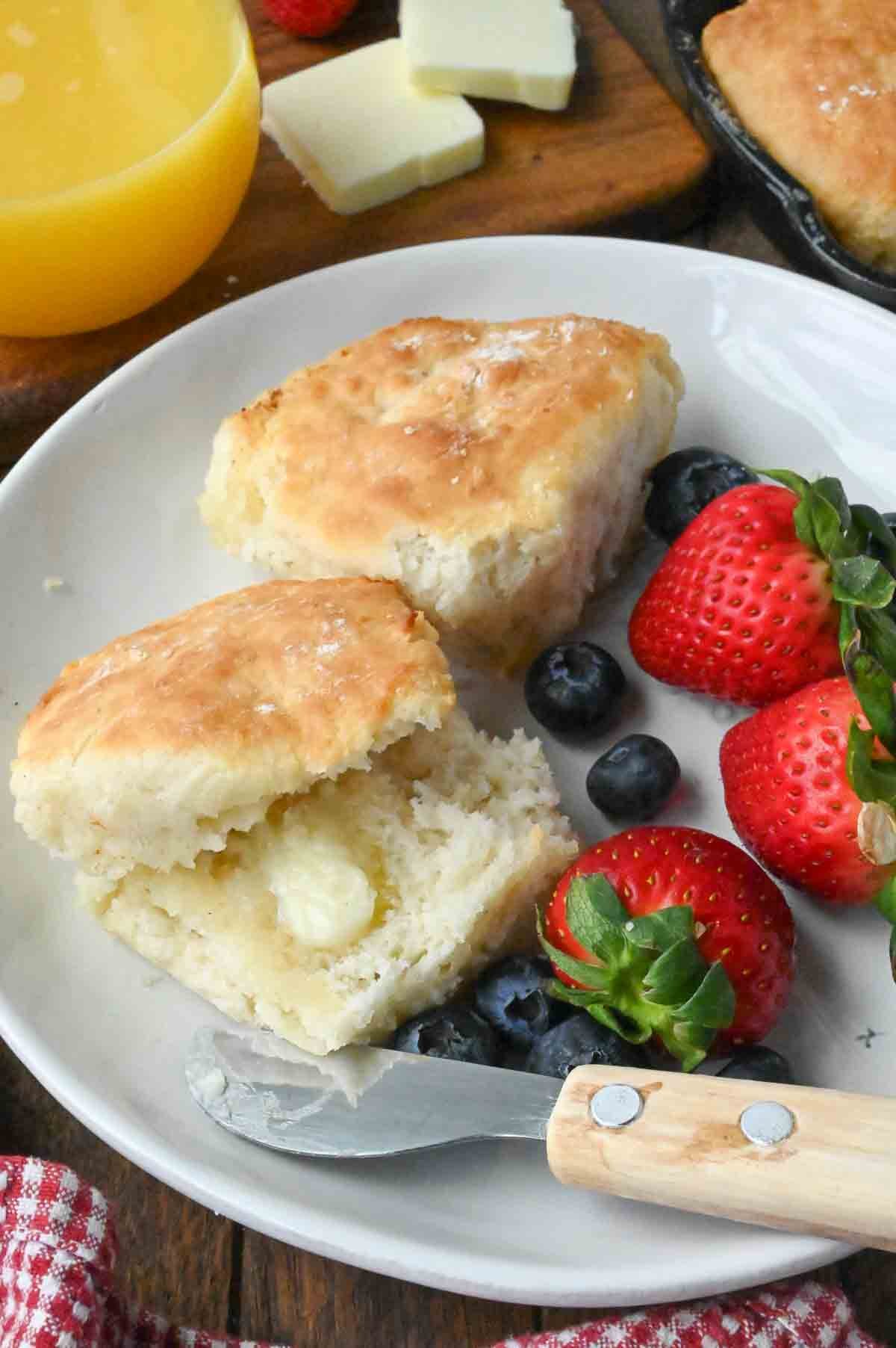 A plate with two 7-up biscuits with a side of strawberries and blueberries.