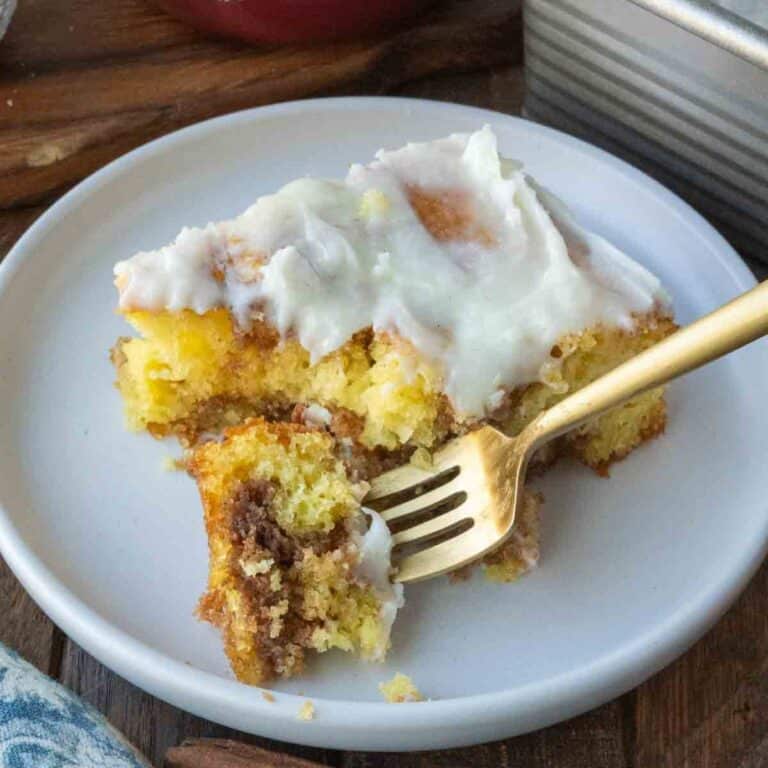 A plate with a golden fork and a slice of cinnamon roll cake with frosting.