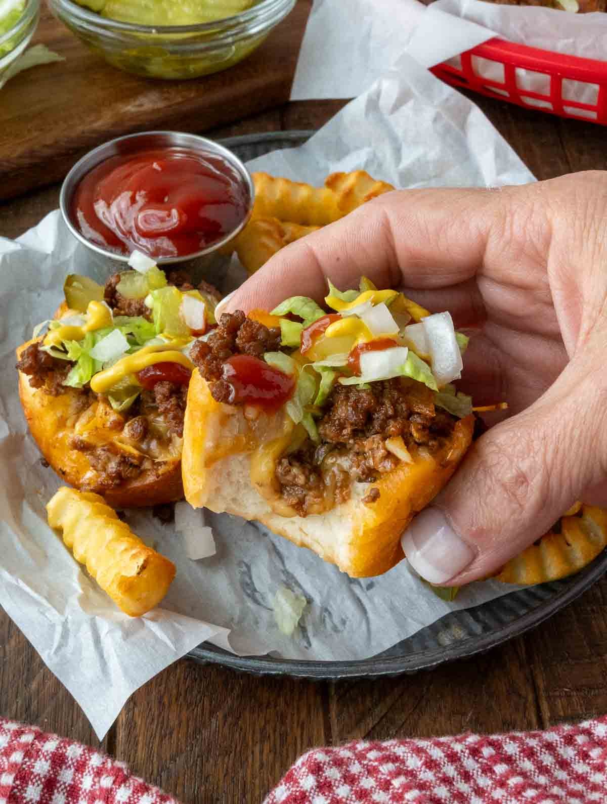 Holding up a single cheeseburger cup piled high with toppings.