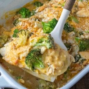 Taking a scoop of broccoli cheddar chicken from a baking dish.