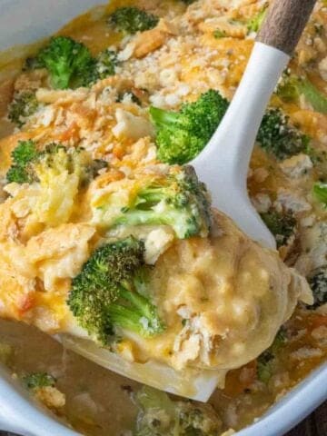 Taking a scoop of broccoli cheddar chicken from a baking dish.