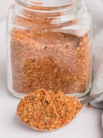 A glass jar filled with tex mex seasoning and a spoon with a heap of seasoning on it.