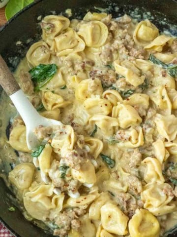 Stirring creamy sausage tortellini in a skillet.