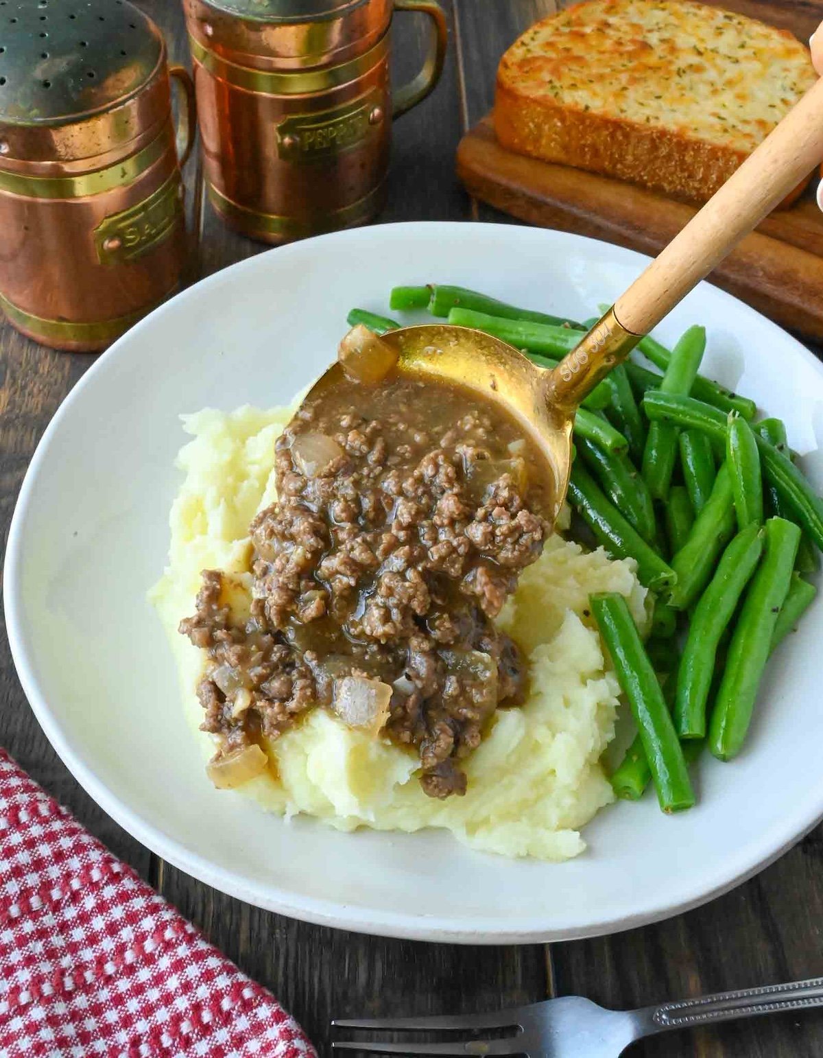 Spooning ground beef and gravy over mashed potatoes.