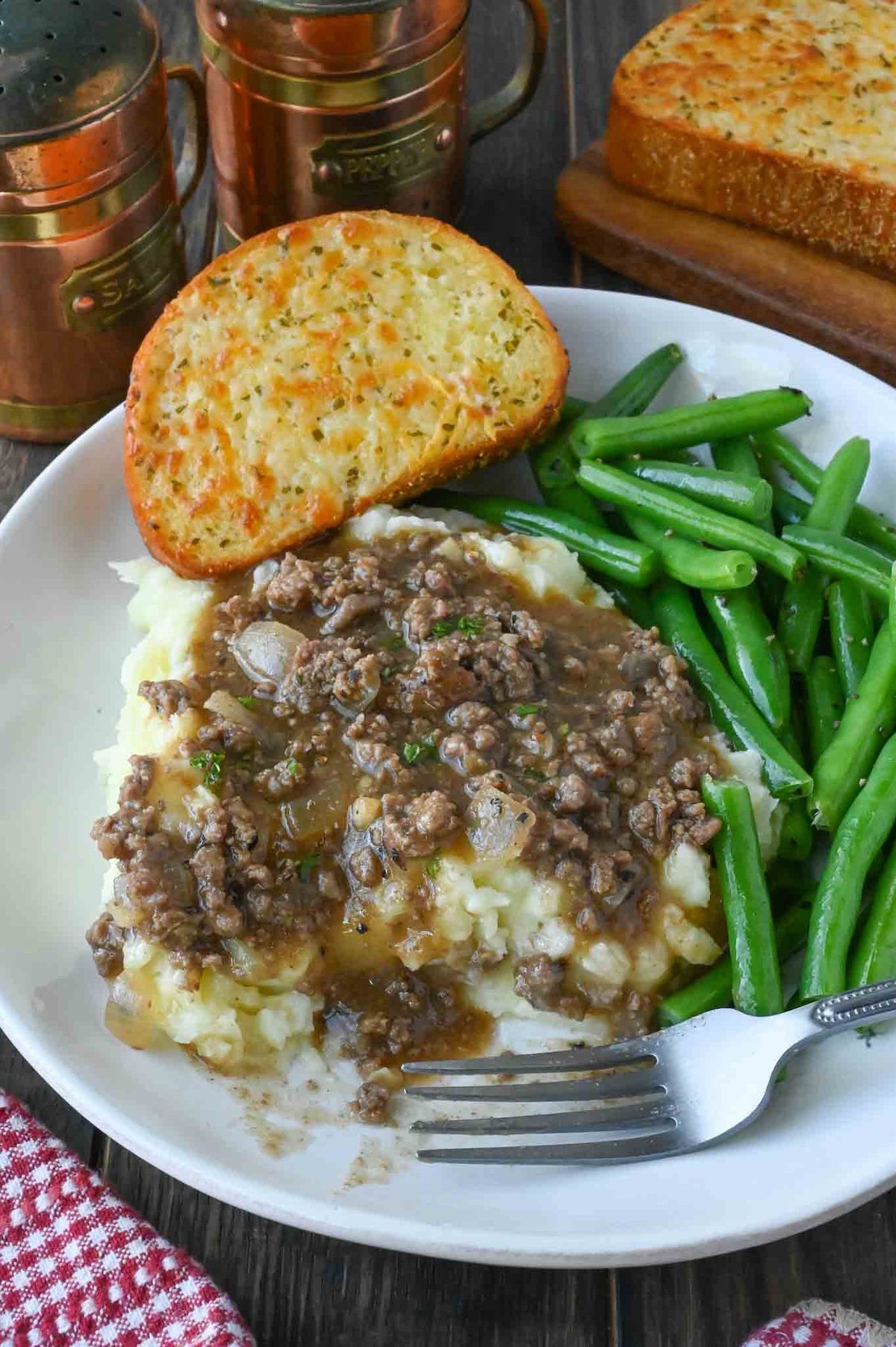 Ground beef and gravy over mashed potatoes with a side of green beans and texas toast.