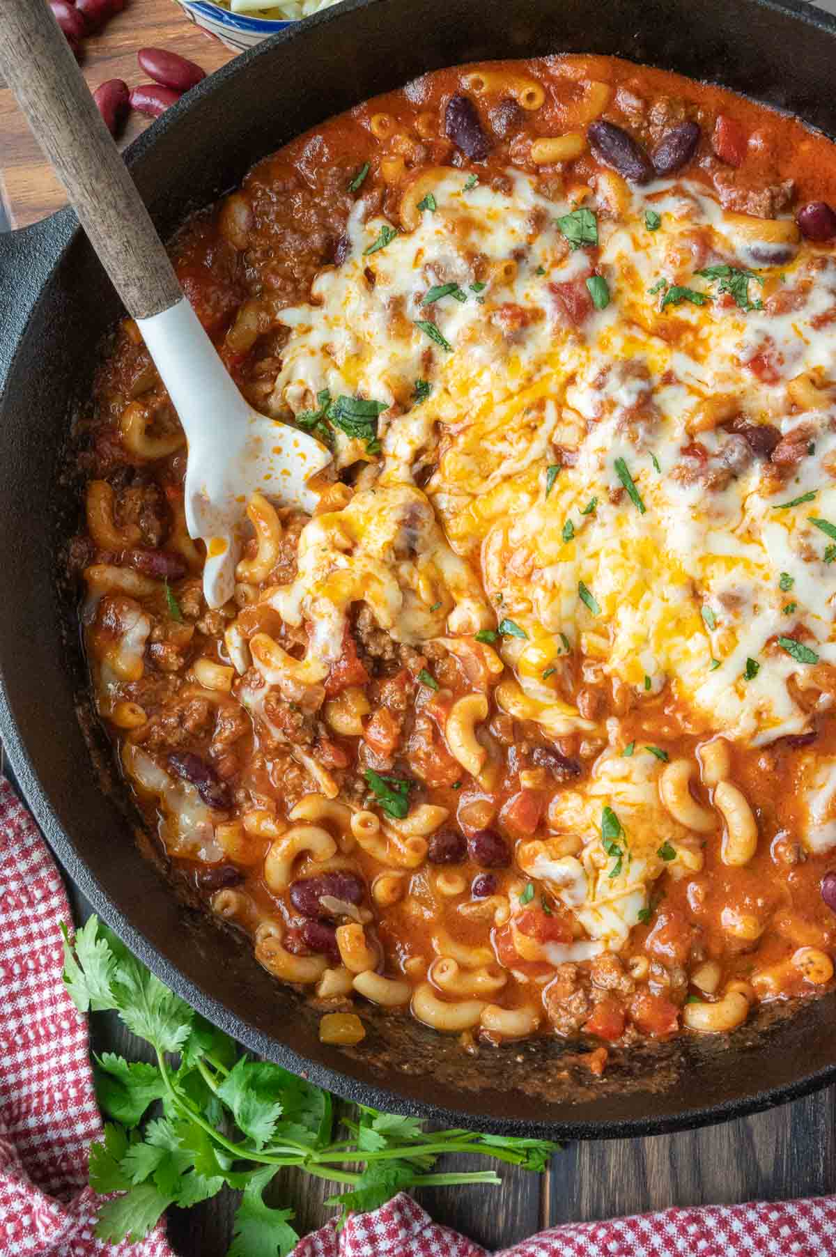 A serving spoon in a skillet of chili mac.