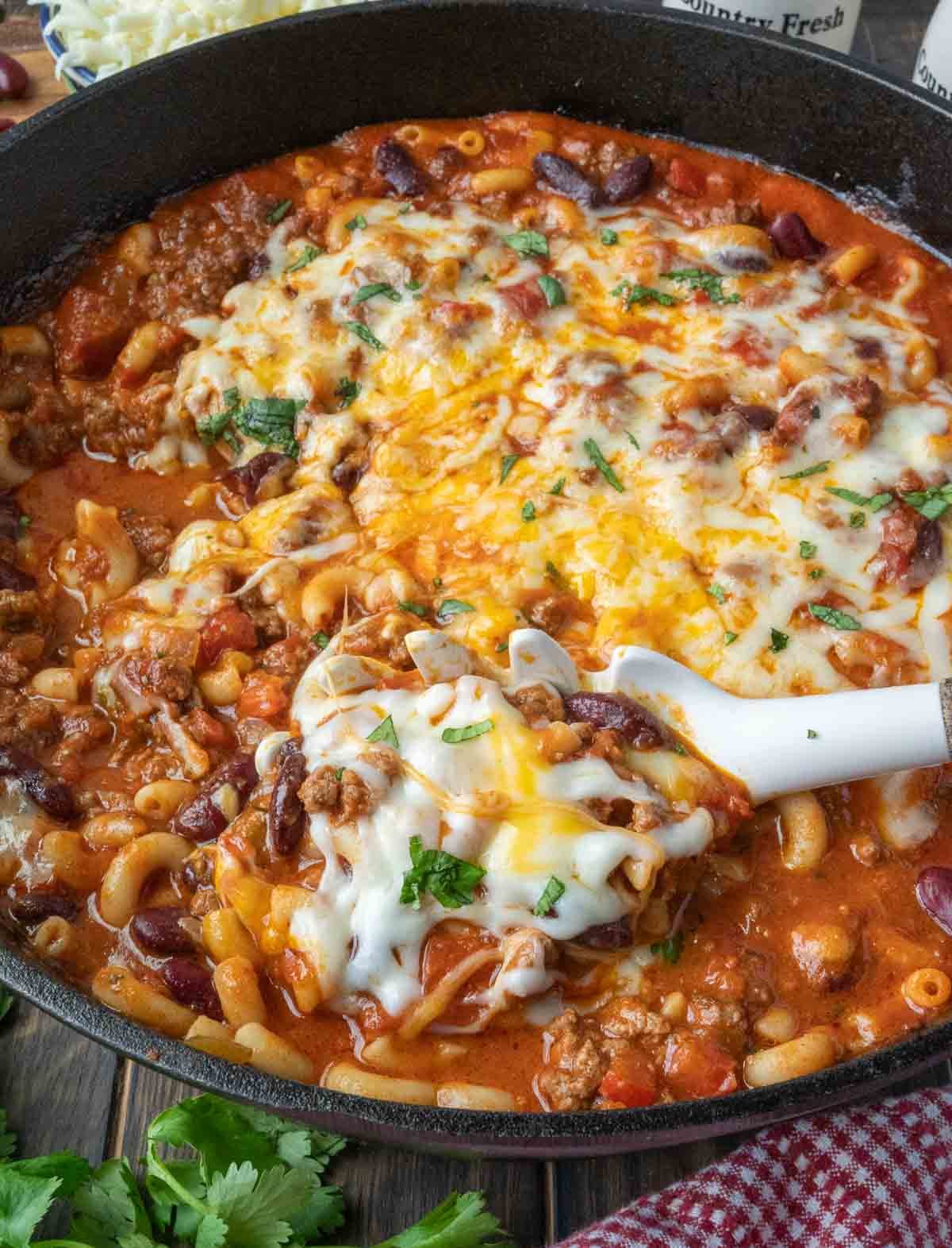Chili mac in a skillet with a serving spoon.