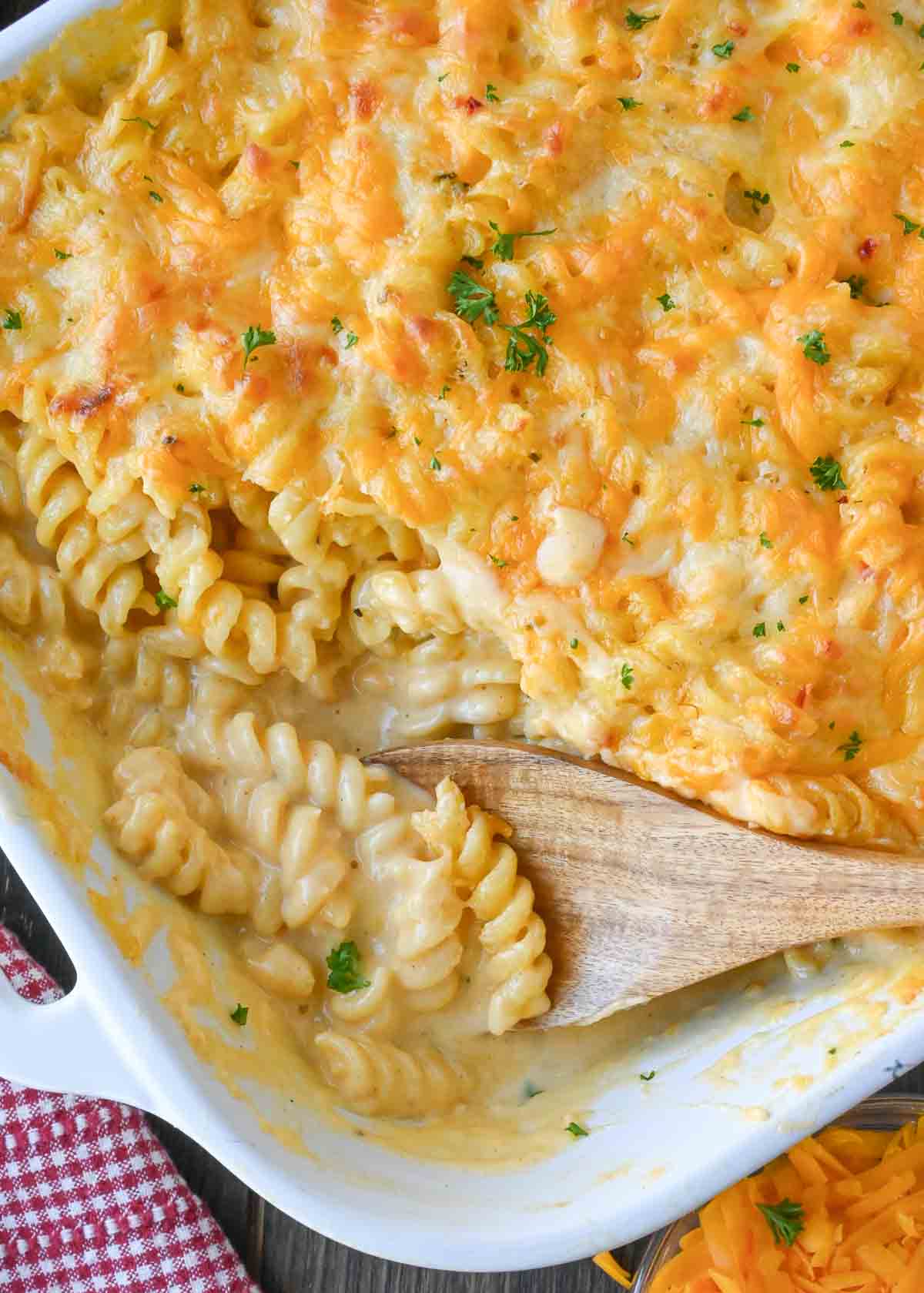 A wooden spoon in a baking dish full of 5 cheese mac and cheese.