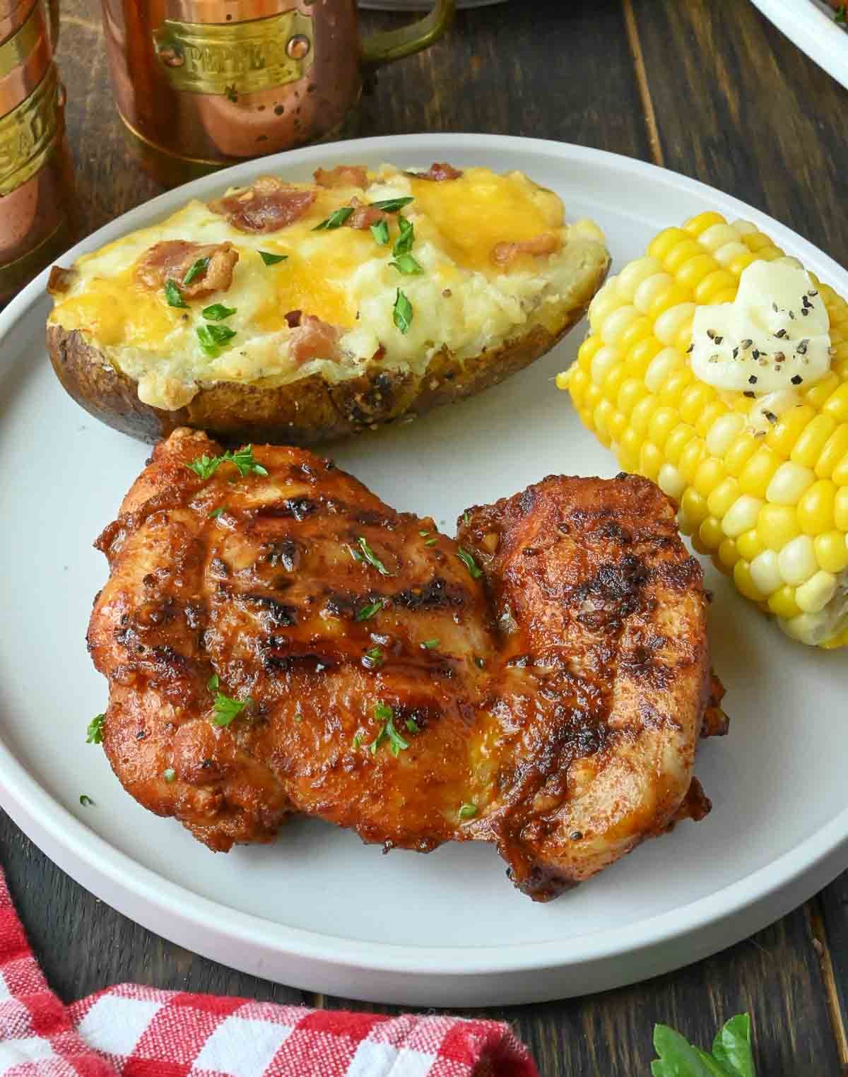Paprika chicken thighs on a plate with twice baked potato and corn on the cob.