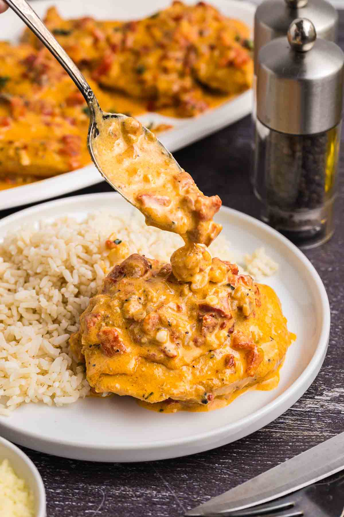 Red pepper sauce poured on top of chicken on a plate.