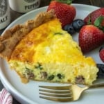 A slice of sausage quiche on a plate with a fork.
