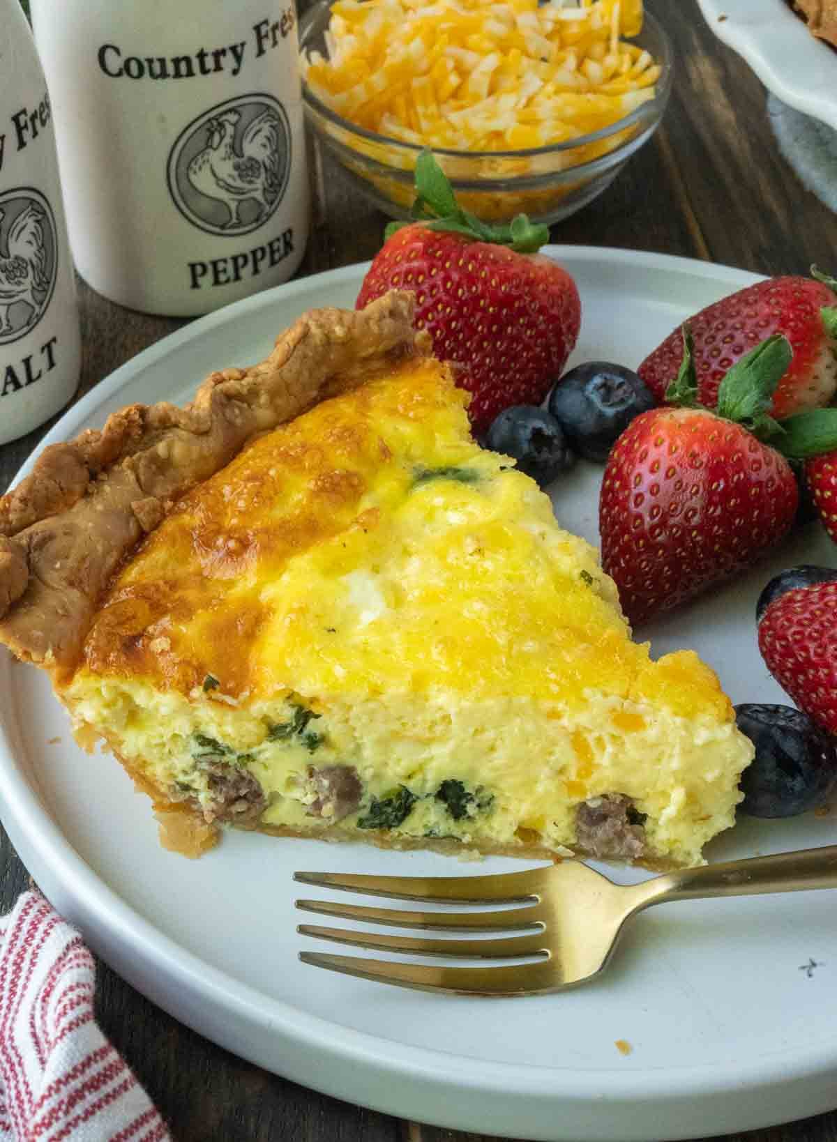 A slice of quiche on a plate with fruit.