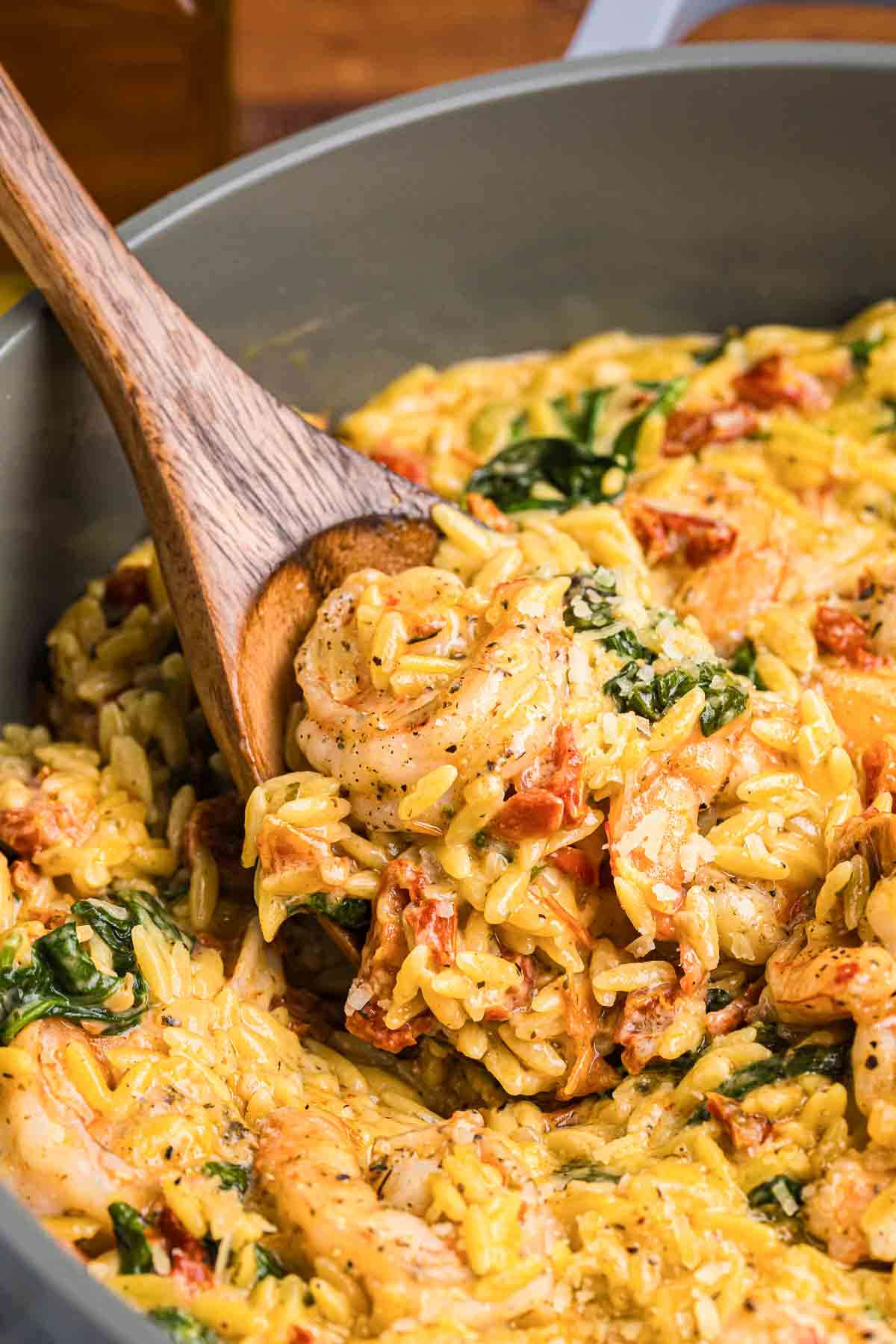 Using a wooden spoon to mix up orzo pasta with shrimp.