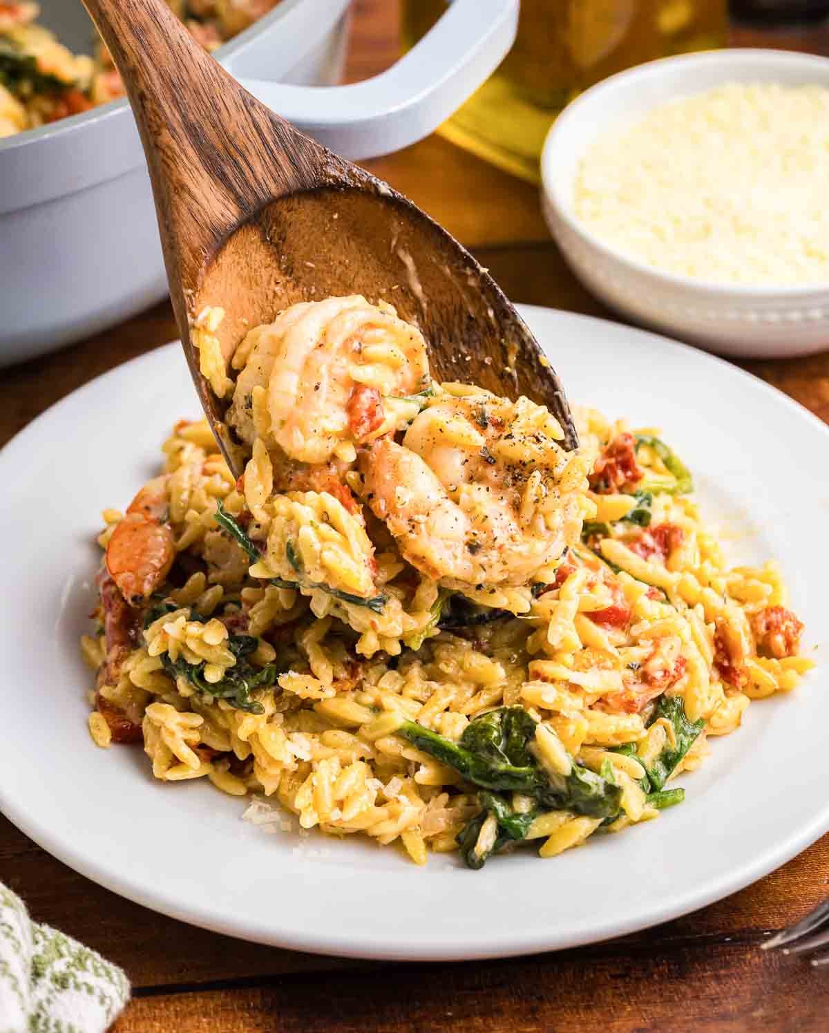Spooning tuscan shrimp orzo skillet onto a plate.