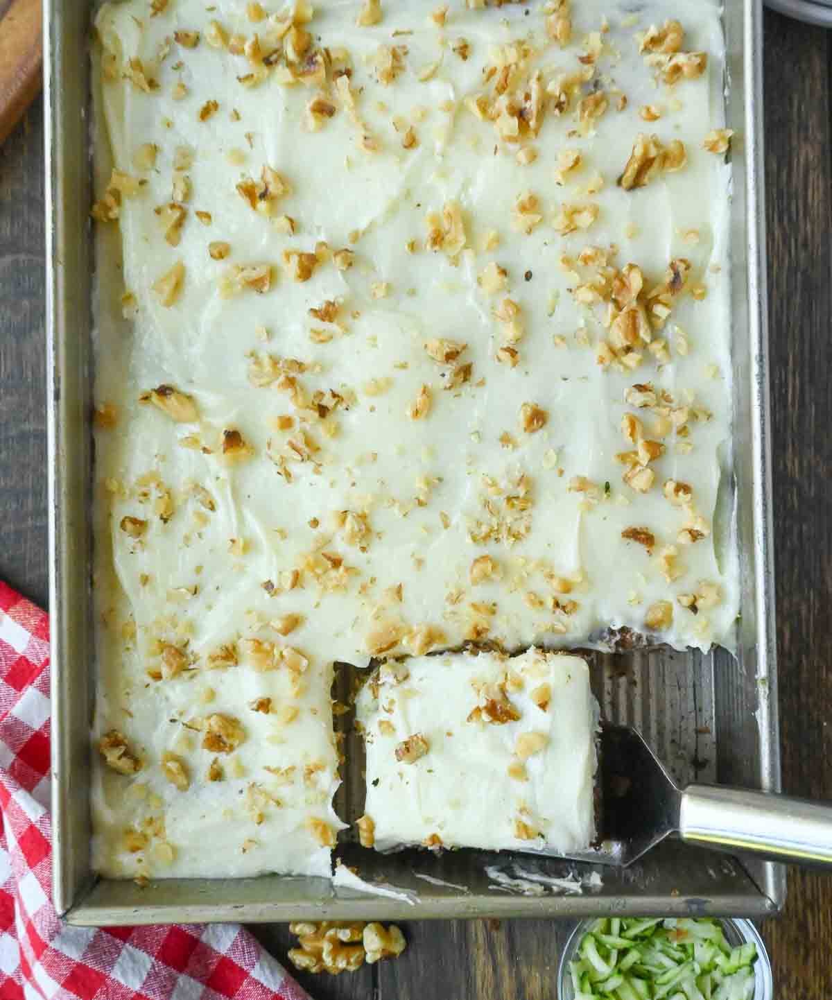 Zucchini cake in a baking pan with a spatula scooping out a slice.