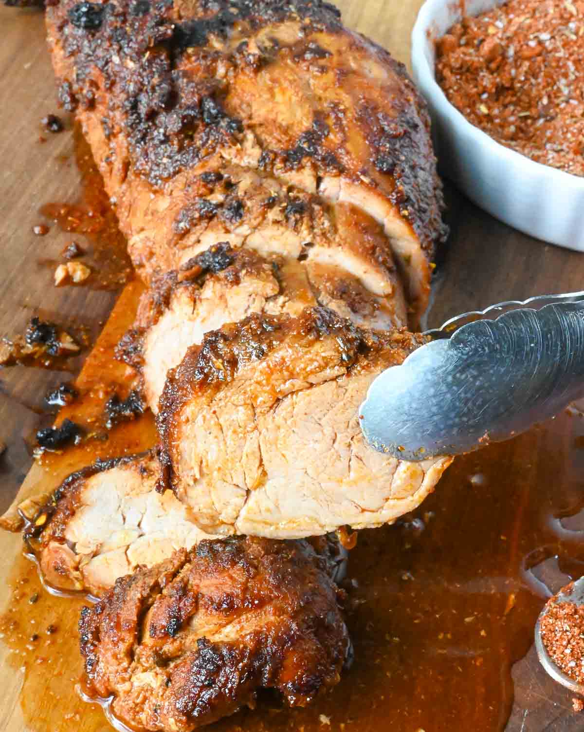 A slice of pork tenderloin being picked up with tongs.