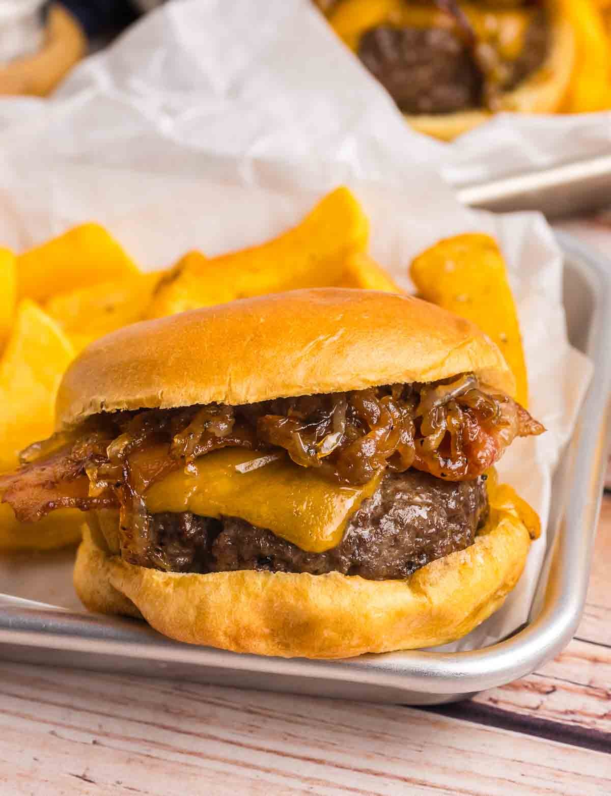 A bourbon bacon cheeseburger on a serving platter with french fries.