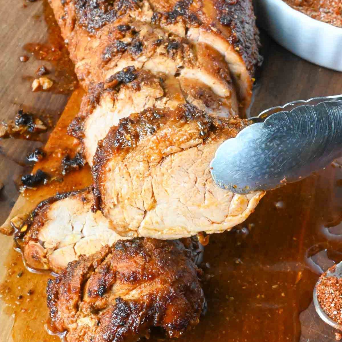 A slice of pork tenderloin being picked up with tongs.