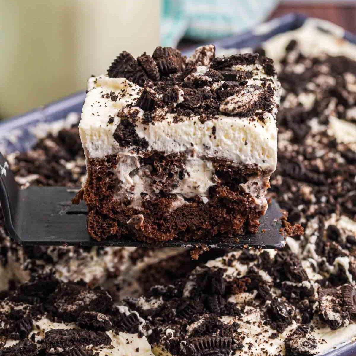 Oreo poke cake slice being picked up with a spatula.