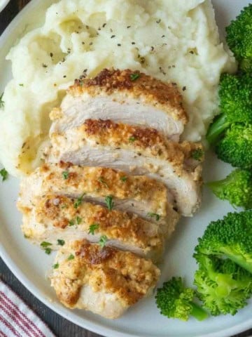 Sliced melt in your mouth chicken on a plate with mashed potatoes and broccoli.
