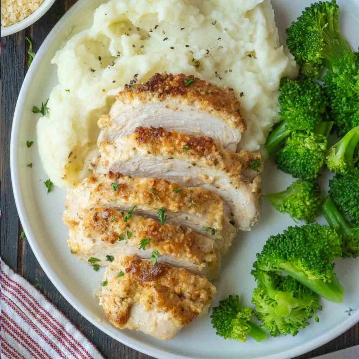 Sliced melt in your mouth chicken on a plate with mashed potatoes and broccoli.