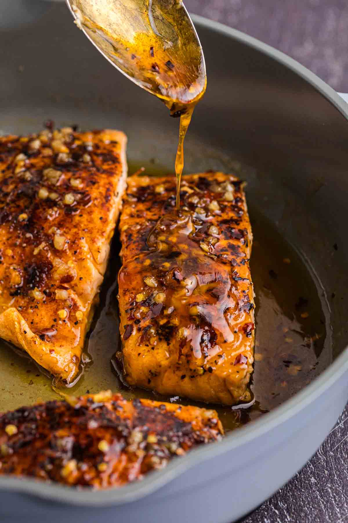 Spooning sauce over a hot honey salmon filet in a skillet.