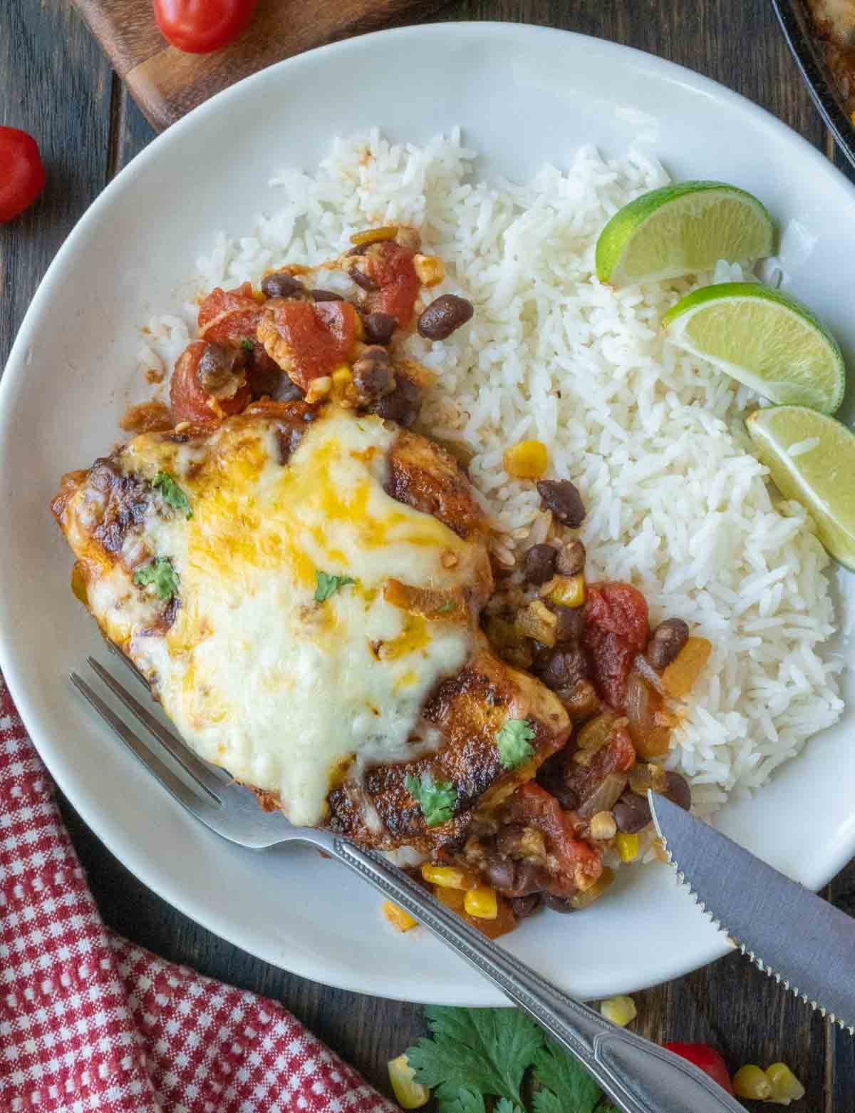 A plate of santa fe chicken served over rice with a side of lime wedges.