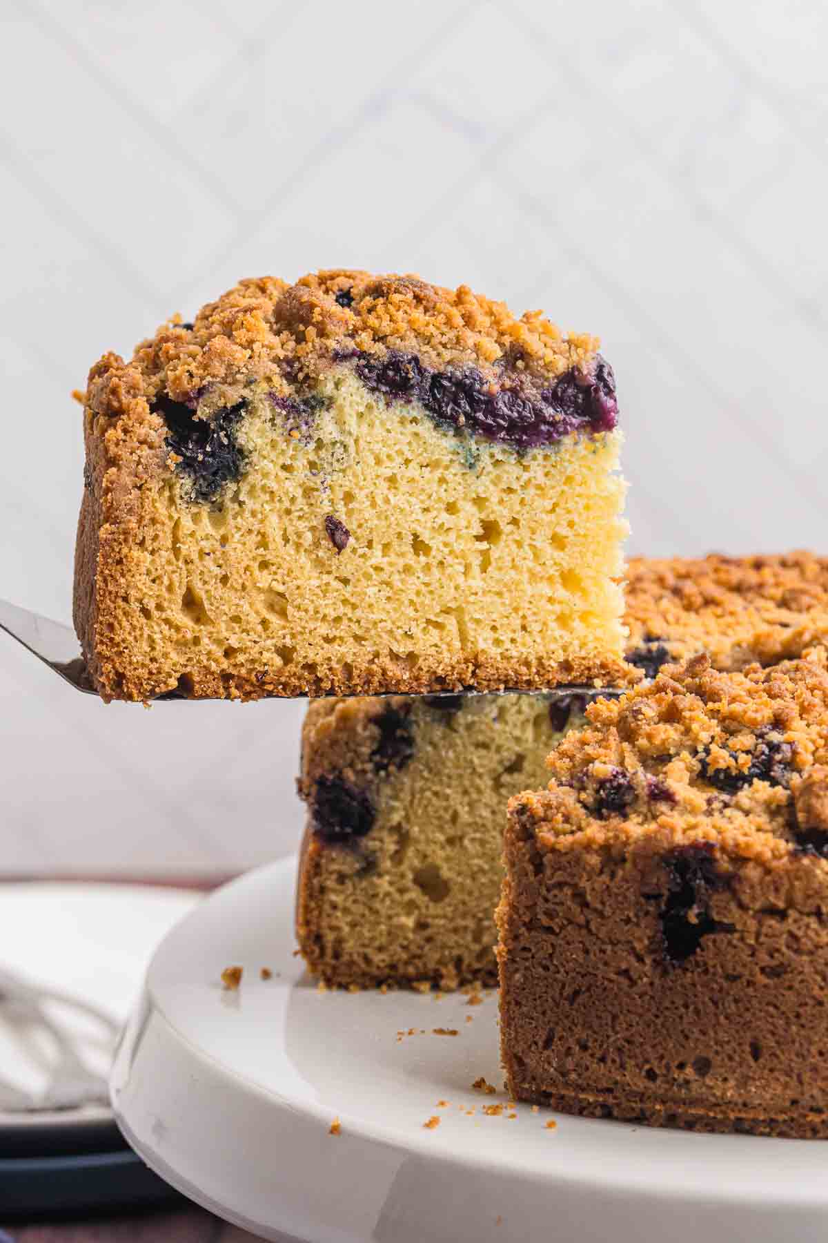 blueberry crumb cake slice being picked up with a spatula.