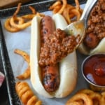 Hot dog chili sauce added to a hot dog with a spoon.