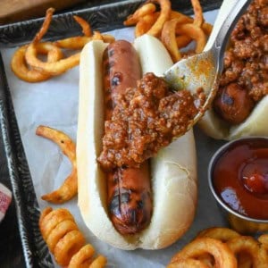 Hot dog chili sauce added to a hot dog with a spoon.