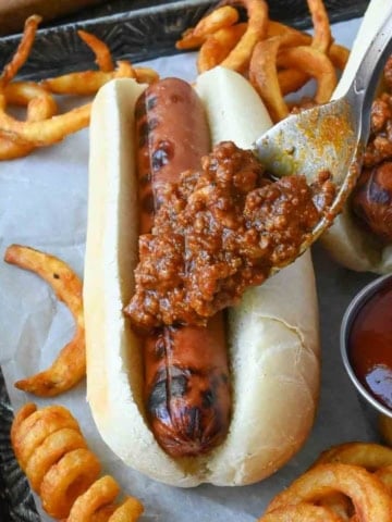 Hot dog chili sauce added to a hot dog with a spoon.
