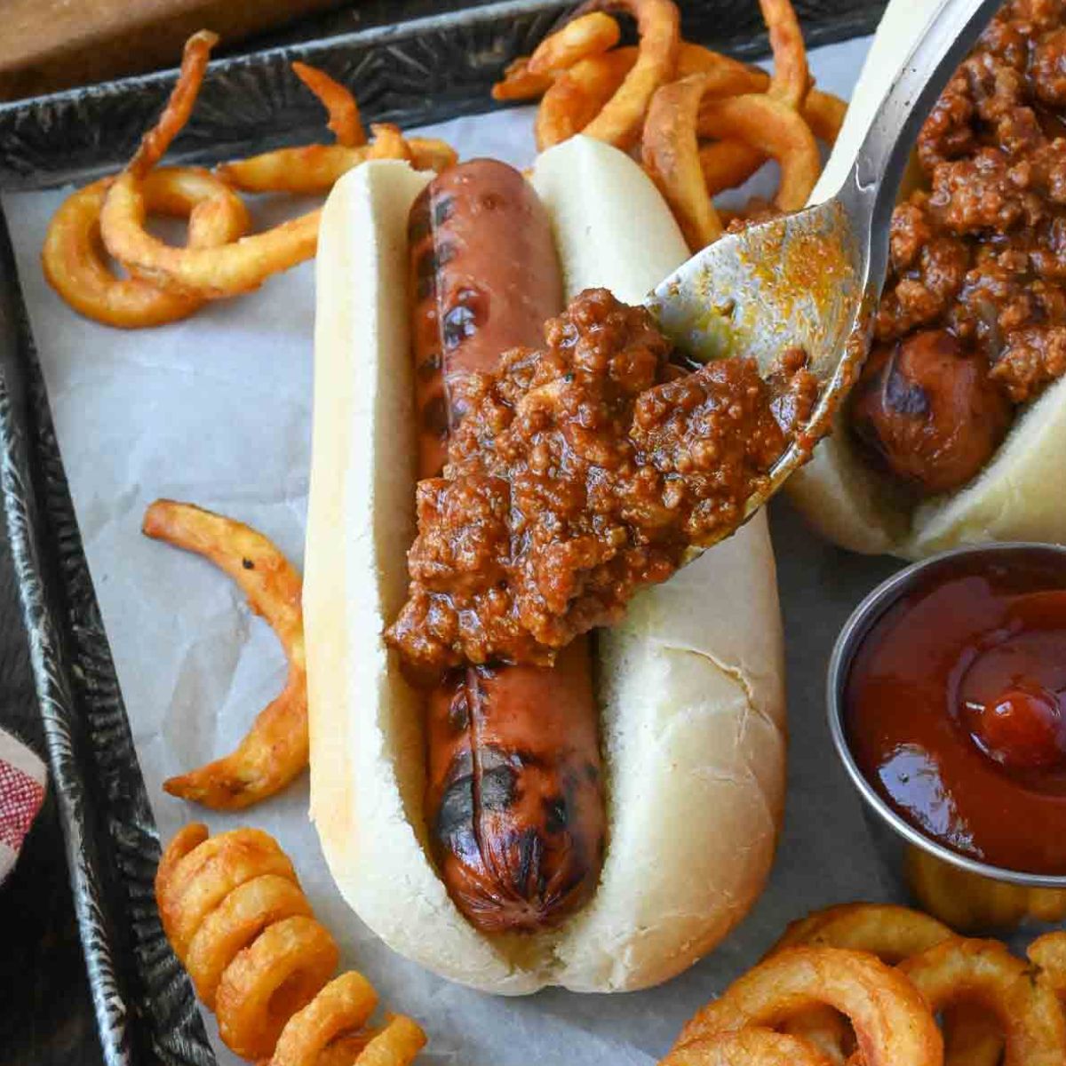 Hot dog chili sauce added to a hot dog with a spoon.