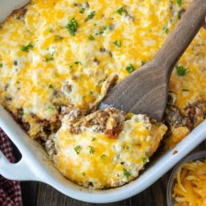 John wayne casserole in a white baking dish with a wooden spoon scooping some out.