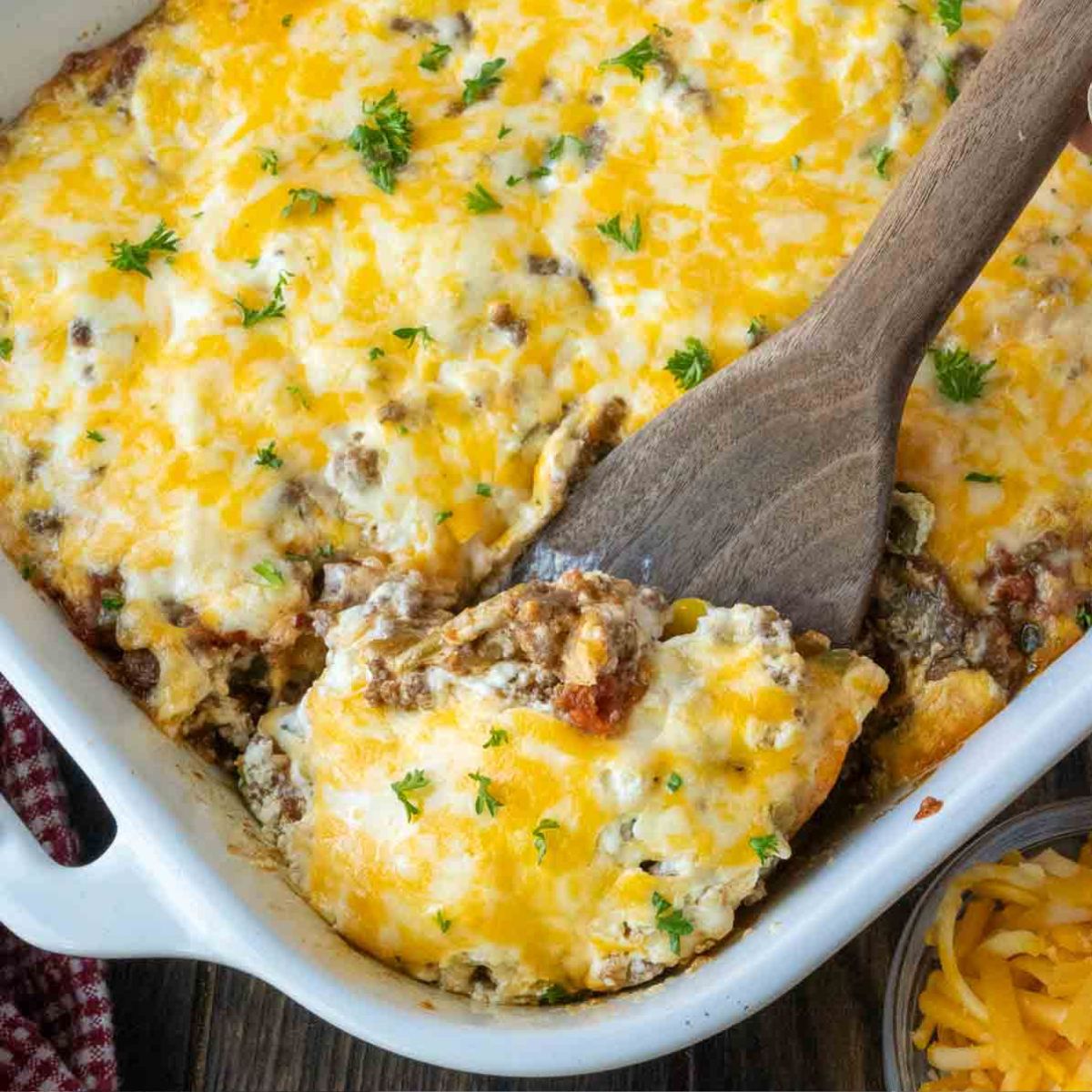 John wayne casserole in a white baking dish with a wooden spoon scooping some out.