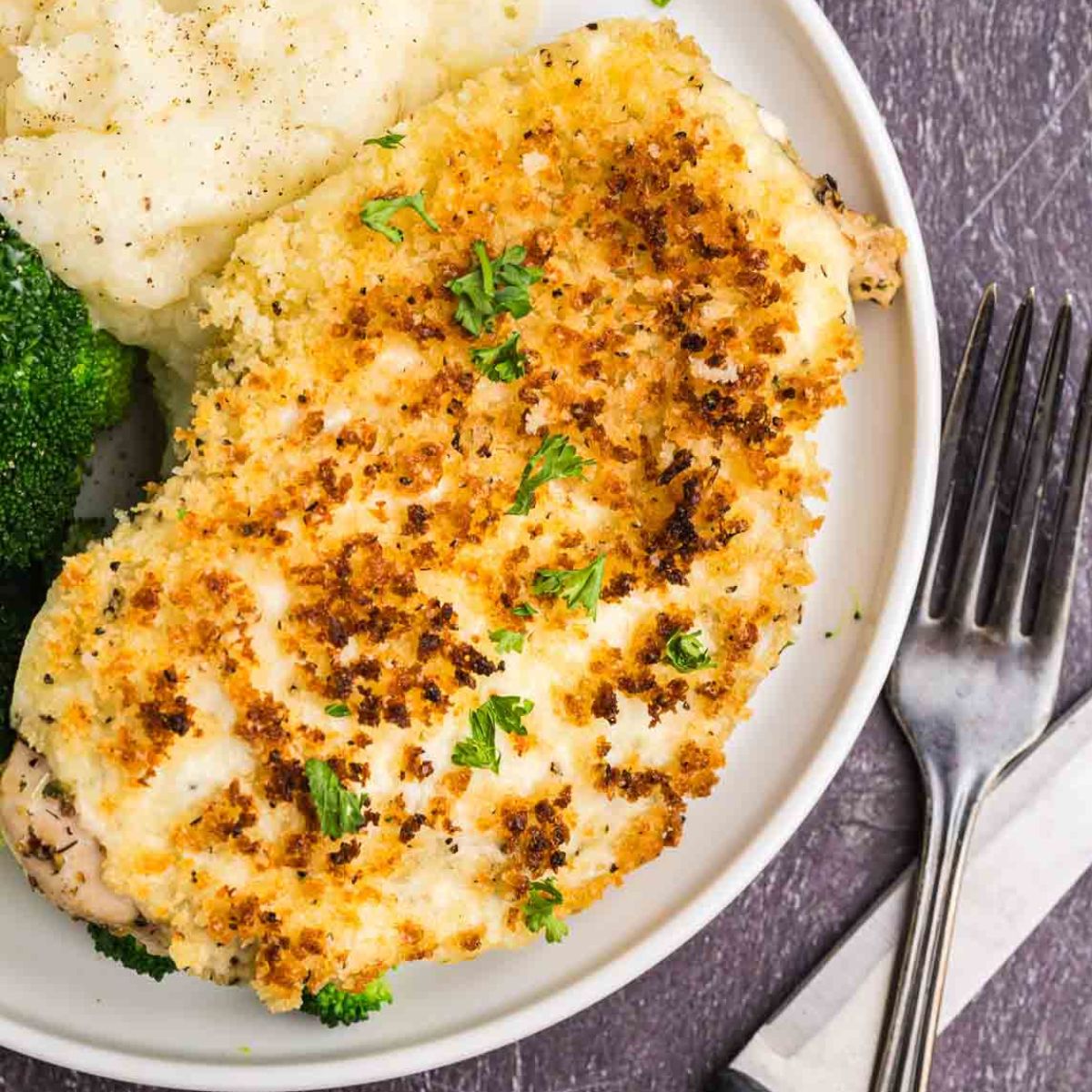 A plate of parmesan crusted chicken with potatoes and broccoli.