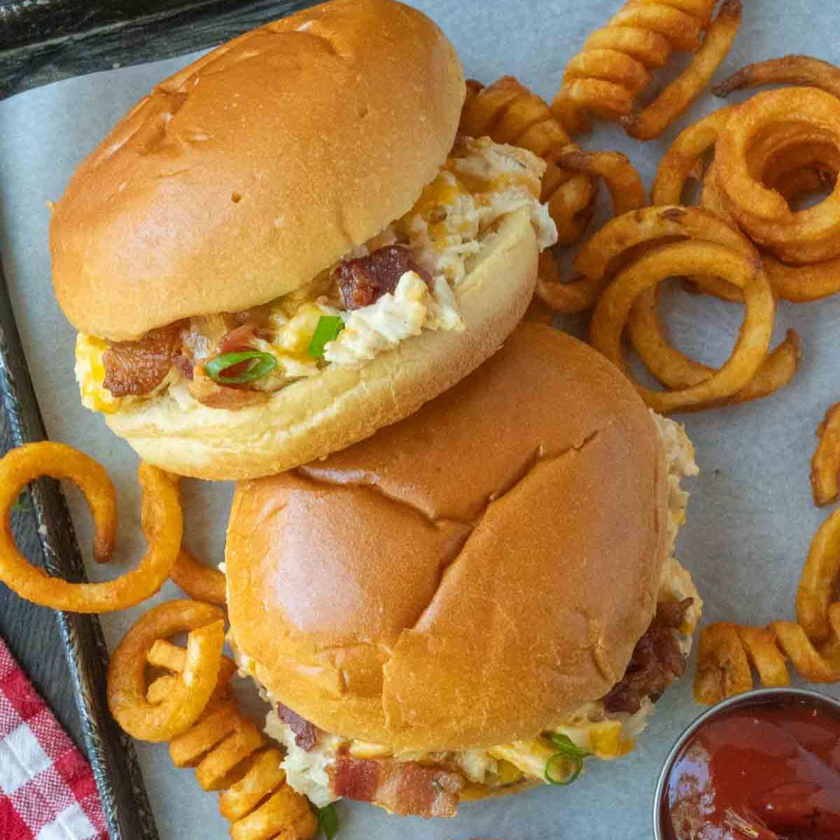 Two bacon ranch sandwiches on a pan with curly fries.