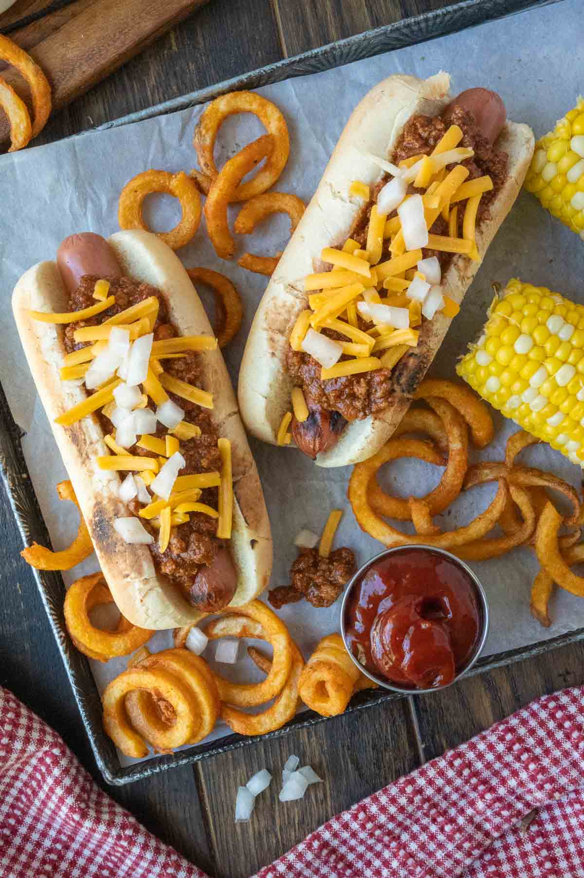 Two hot dogs with chili sauce and curly fries.