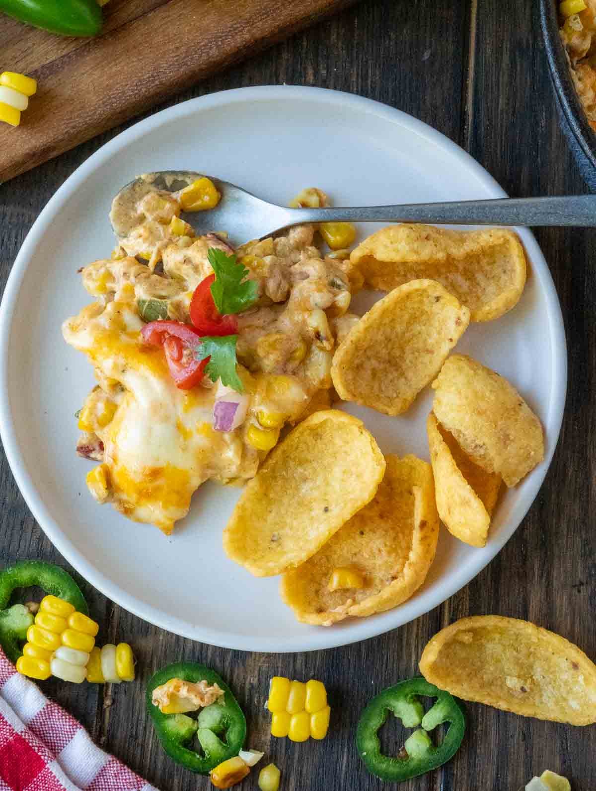 A plate with jalapeno corn dip and corn chip scoops.