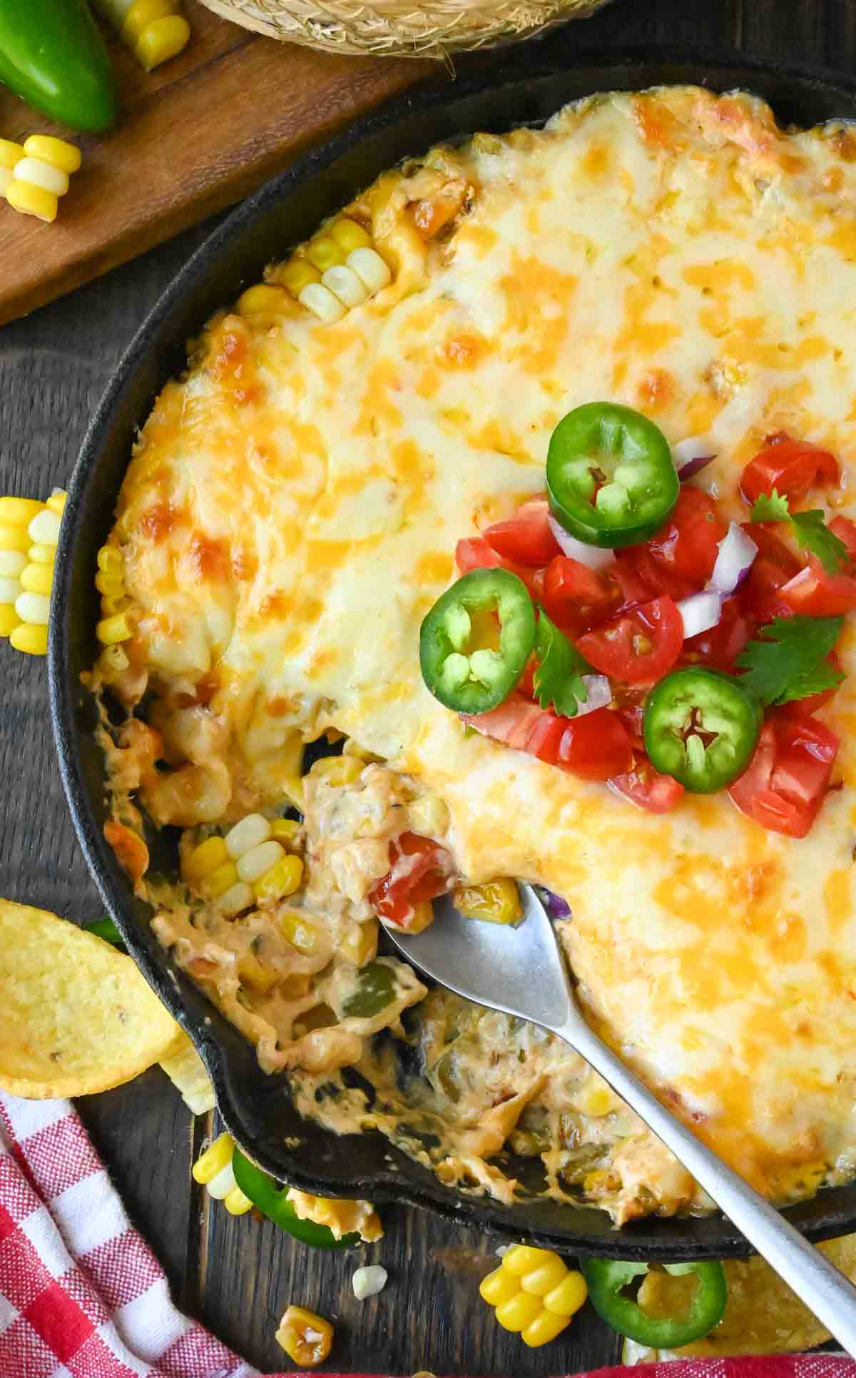 A spoon in a skillet full of jalapeno corn dip.