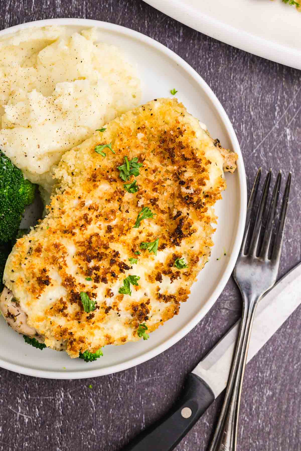 A plate of parmesan crusted chicken with mashed potatoes and broccoli.