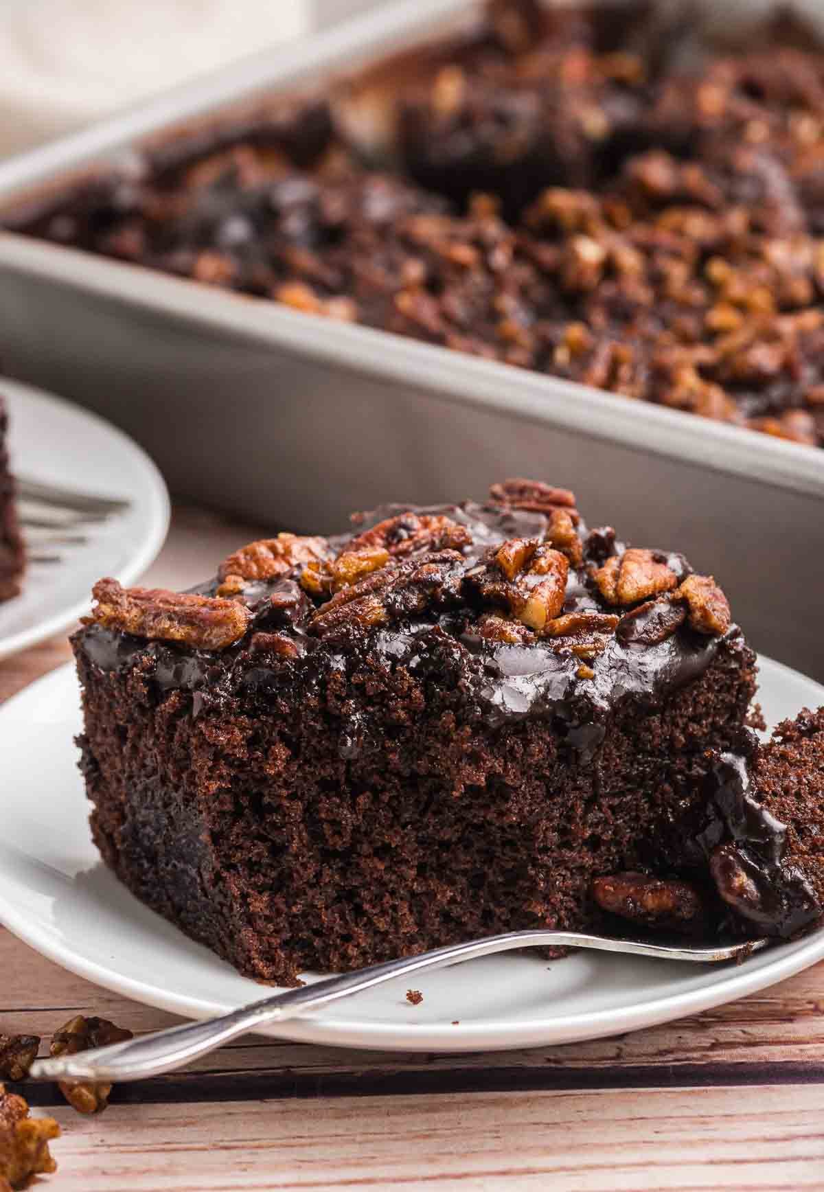A plate of dr pepper cake with the rest of the cake in the background.