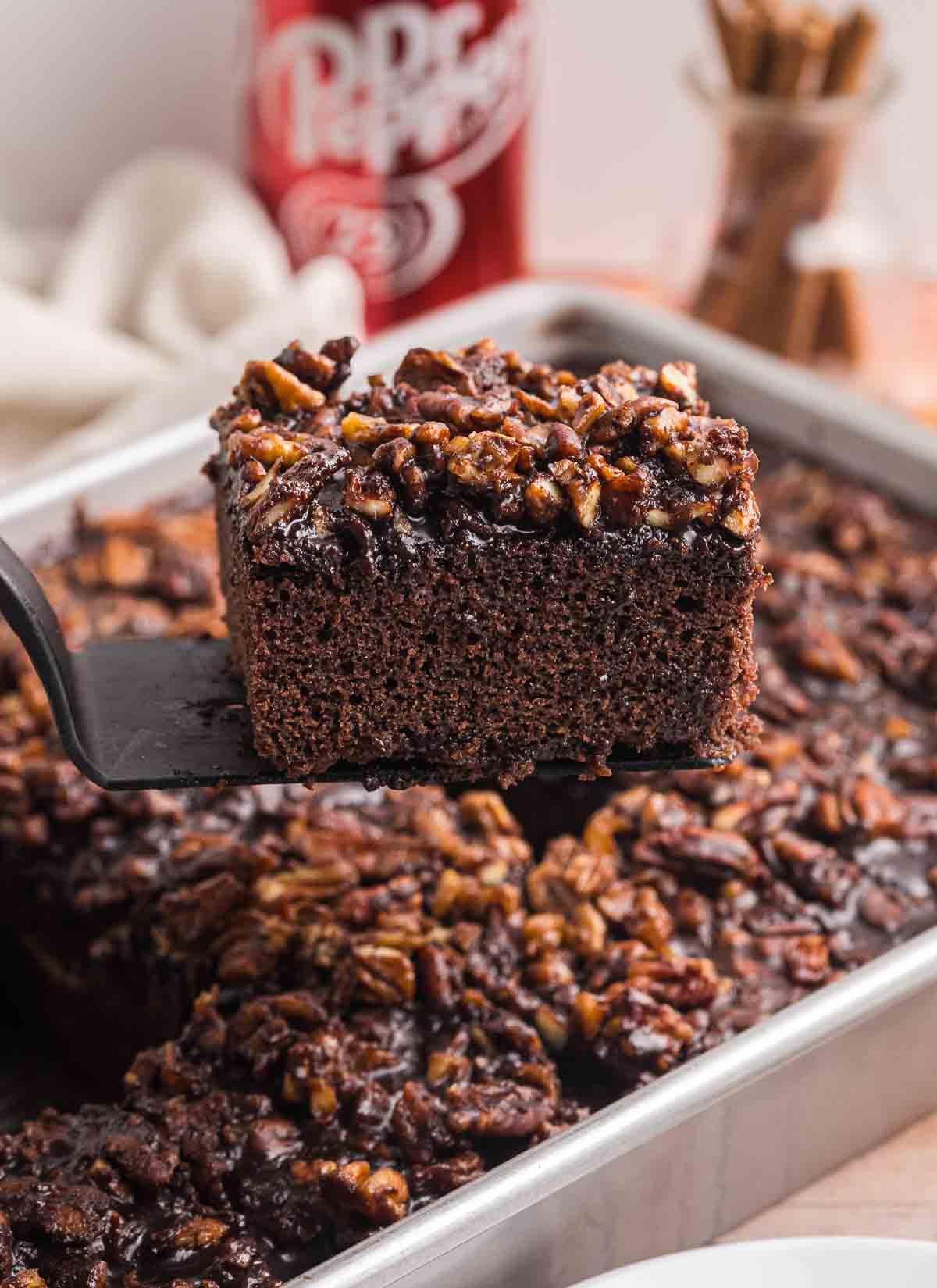 Using a spatula to lift a slice of dr pepepr cake out of a baking dish.