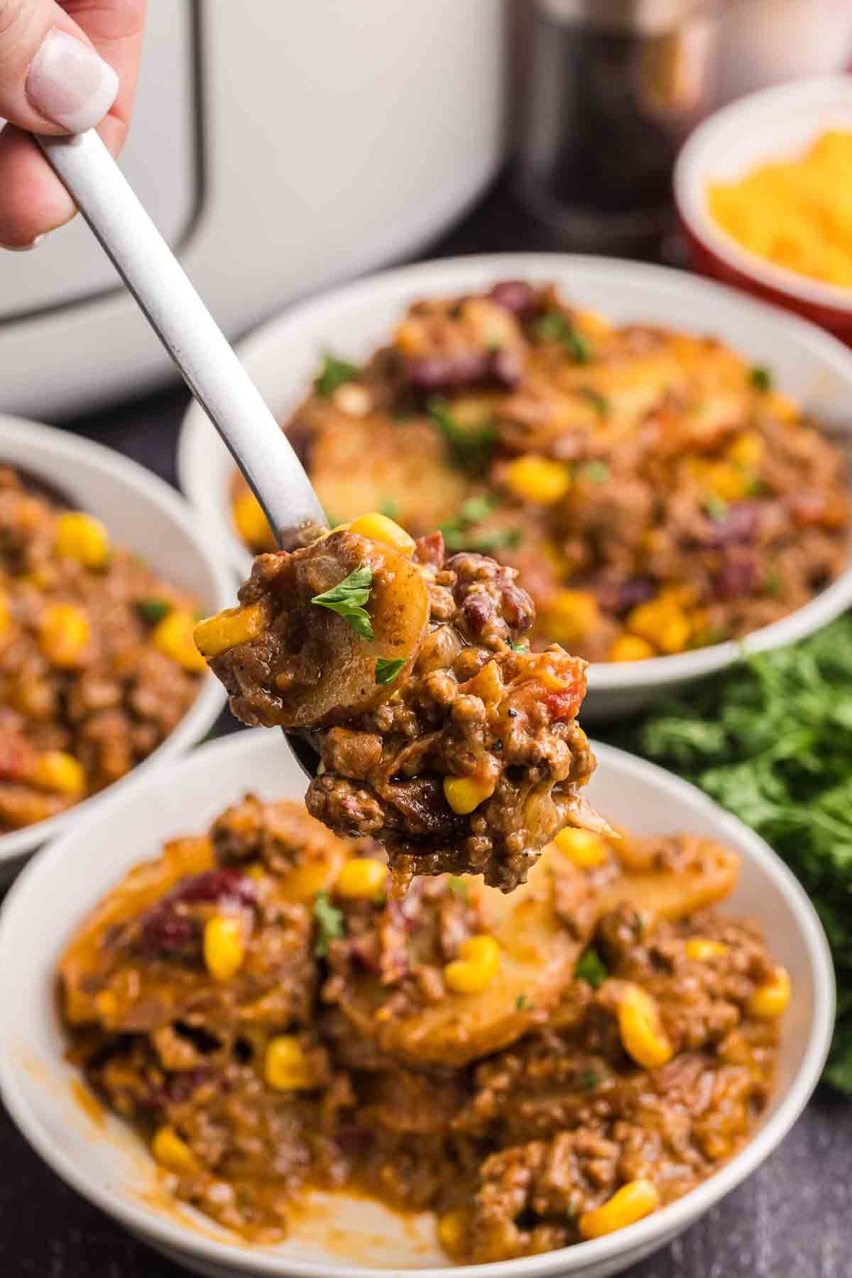 Spooning slow cooker cowboy casserole into a bowl.