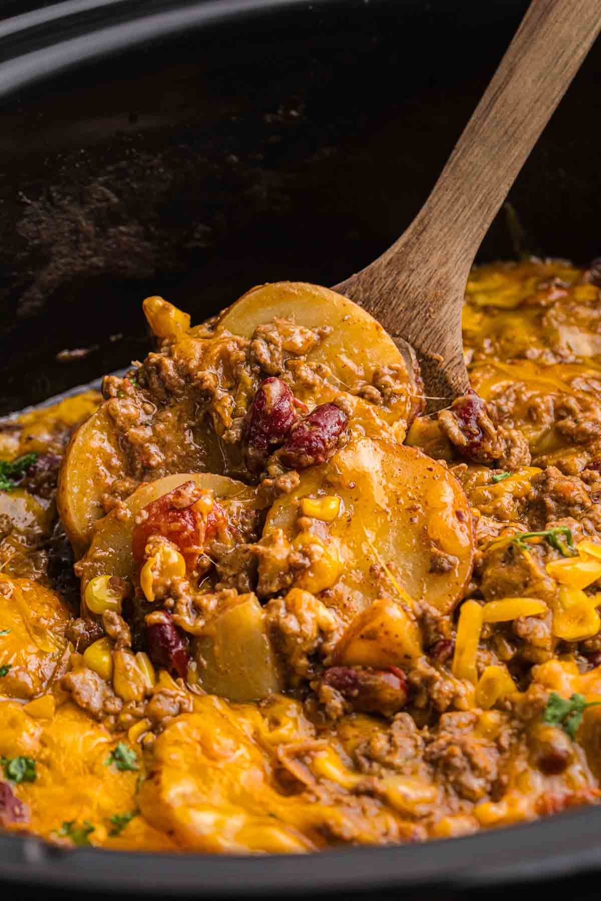Using a wooden spoon to stir cowboy casserole in the slow cooker.