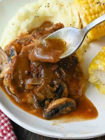 Spooning gravy over slow cooker smothered chicken.