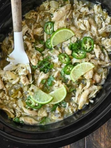 Salsa verde chicken in the slow cooker with lime slices and jalapenos.