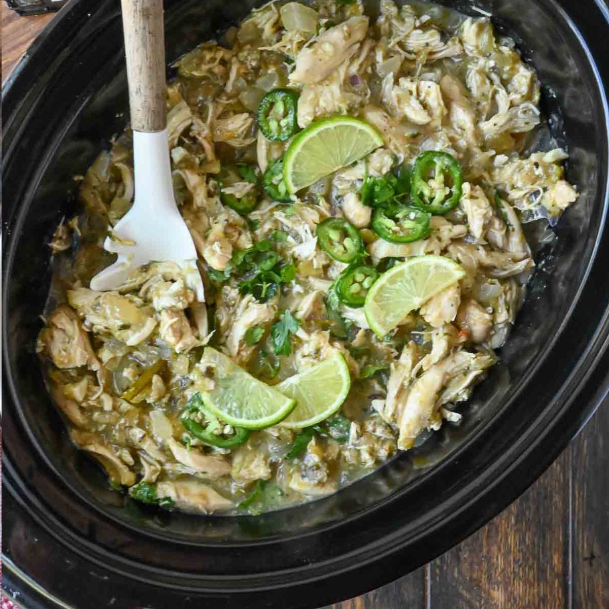Salsa verde chicken in the slow cooker with lime slices and jalapenos.