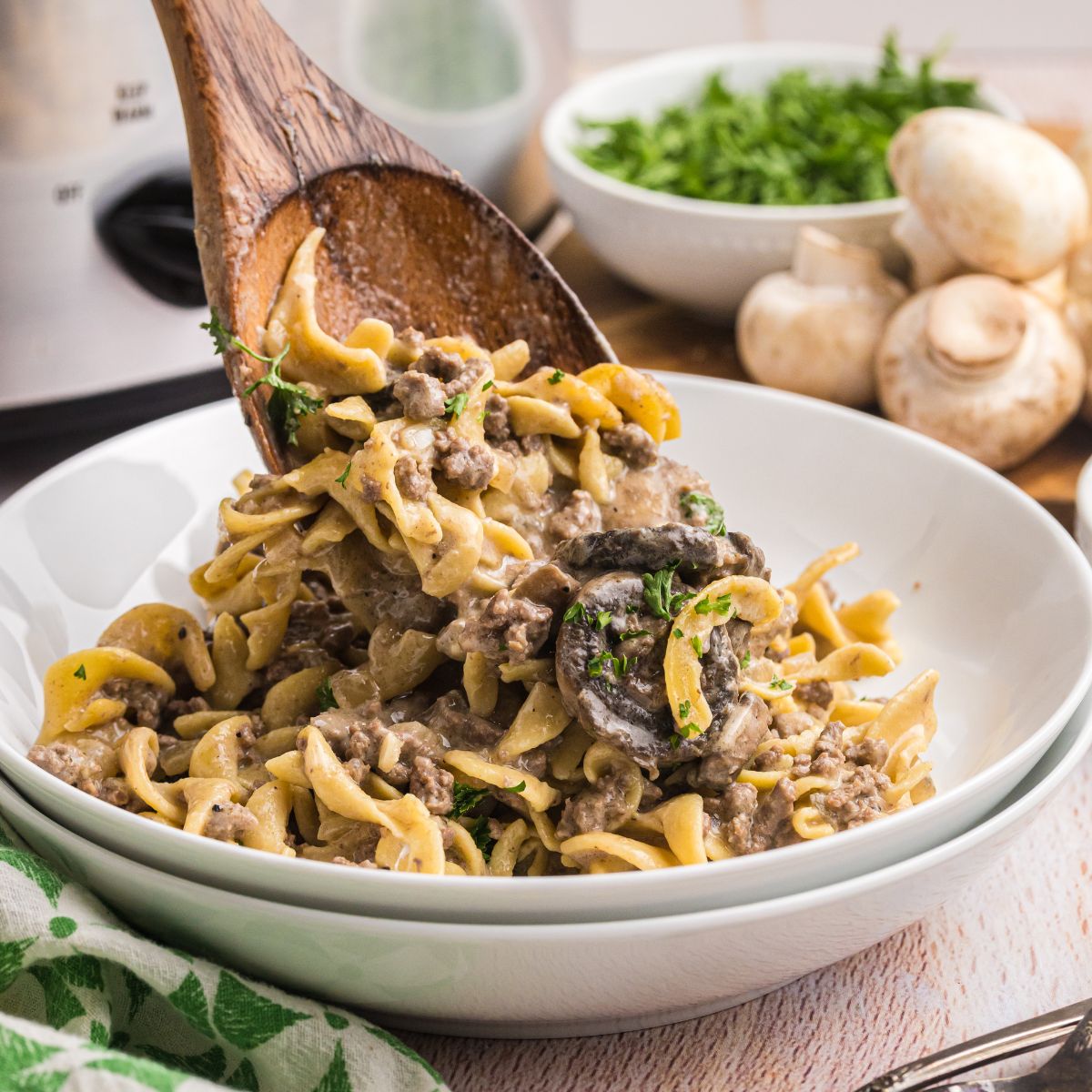 Spooning slow cooker beef stroganoff into a white bowl.
